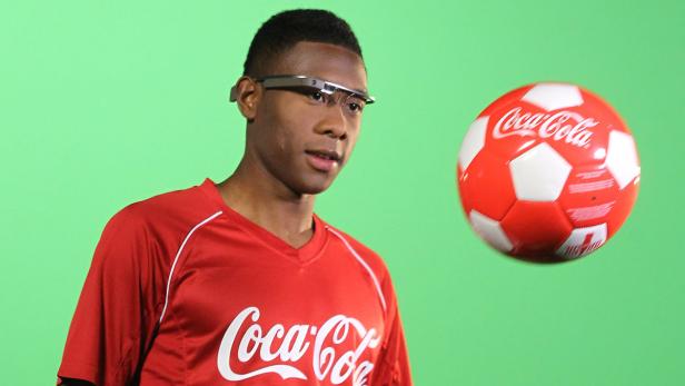 Ein Mann mit Brille und Coca-Cola-Trikot jongliert einen Fußball.