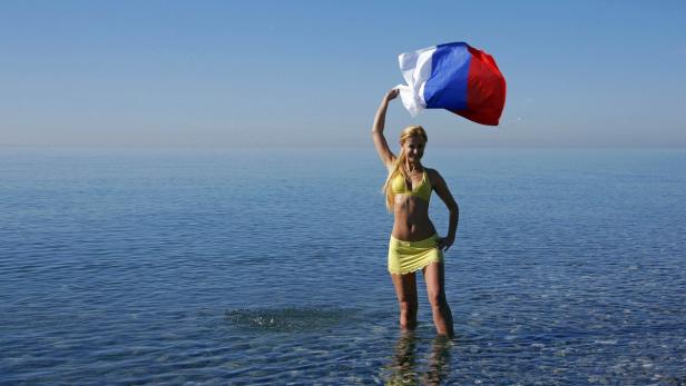Eine Frau steht im Wasser und hält eine russische Flagge hoch.