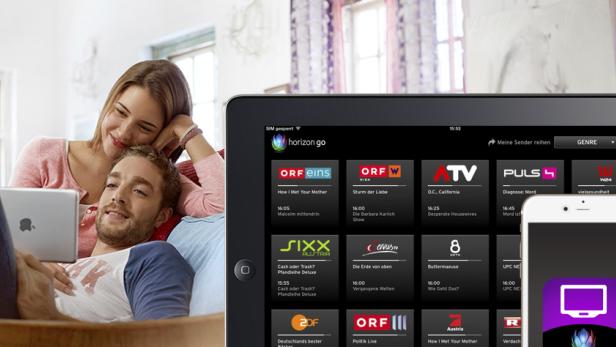 Ein Paar entspannt auf der Couch und schaut mit Tablets und Smartphone „Horizon Go“.