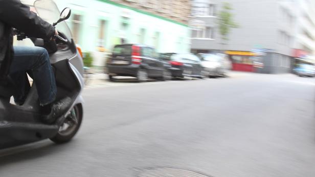 Eine Person fährt mit einem Motorroller eine Straße entlang.