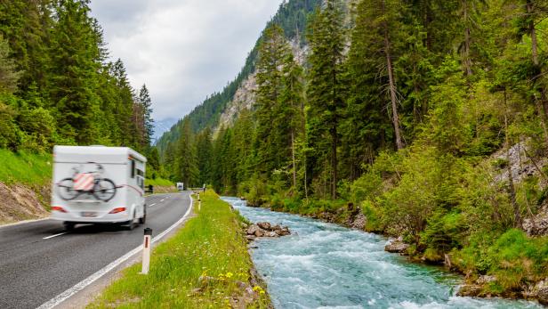 Camper van with attached bicycle driving through the European Alps on a rainy day