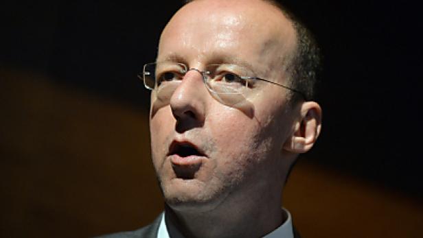 Ein Mann mit Brille spricht vor einem dunklen Hintergrund.