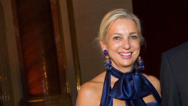 Eine Frau mit blonden Haaren und einem blauen Kleid lächelt in die Kamera.