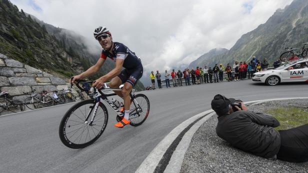 Ein Radfahrer fährt eine kurvenreiche Bergstraße hinauf, während Zuschauer und ein Fotograf die Szene beobachten.