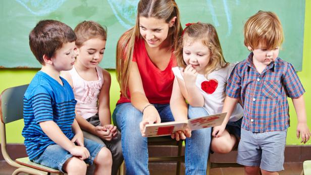 Glückliche Kinder mit Erzieher lesen gemeinsam ein Buch im Kindergarten