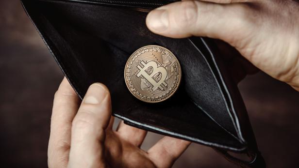 Eine Bitcoin-Münze liegt in einem leeren, schwarzen Portemonnaie.