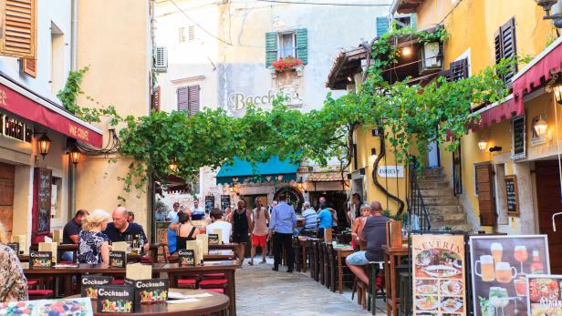 In einer Gasse sitzen Menschen in Restaurants unter Weinreben.