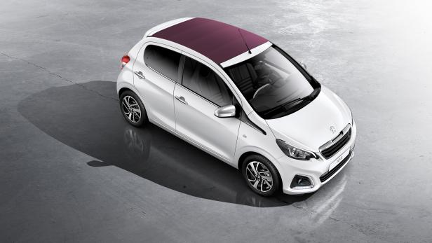Ein weißer Peugeot 108 mit einem burgunderroten Dach auf einer Betonfläche.