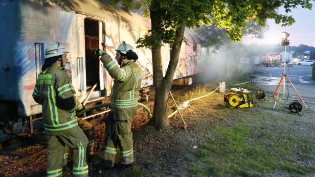 Feuerwehrleute stehen vor einem brennenden Zugwaggon.