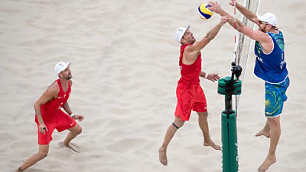 Zwei Beachvolleyballspieler springen am Netz, um einen Ball zu blocken.