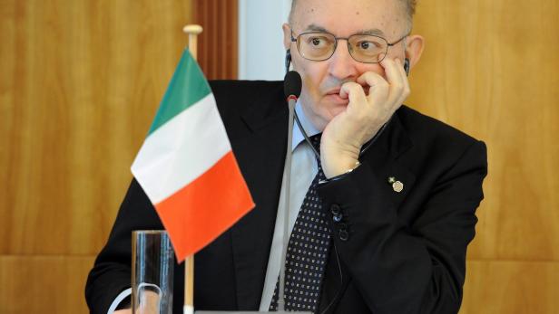 Ein Mann mit Brille sitzt an einem Tisch mit einer italienischen Flagge.