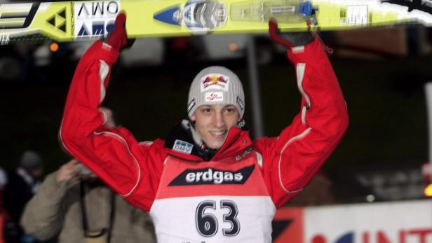 Ein Skispringer mit der Startnummer 63 hält seine Skier über den Kopf.