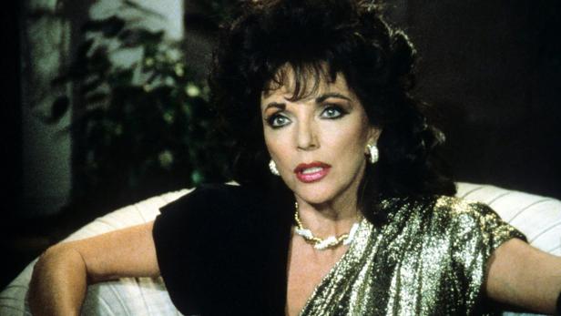 Joan Collins in einem goldenen Kleid und mit auffälligem Schmuck.