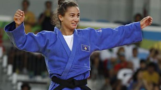 Eine Judoka im blauen Anzug mit der Flagge des Kosovo jubelt.