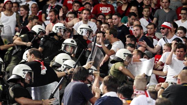 Polizisten in Schutzausrüstung stehen einer Menge von Fußballfans gegenüber.