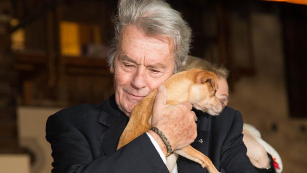 Alain Delon umarmt einen kleinen, hellbraunen Hund.