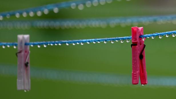 Zwei Wäscheklammern hängen an einer nassen Wäscheleine mit vielen Wassertropfen vor grünem Hintergrund.