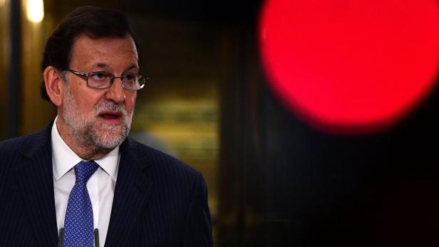Mariano Rajoy bei einer Rede vor einem dunklen Hintergrund mit rotem Licht.