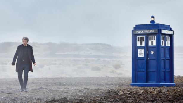 Peter Capaldi als Doctor Who steht neben einer blauen Tardis in einer nebligen Landschaft.