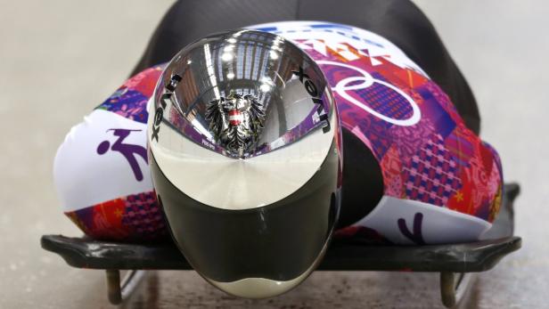 Ein Skeletonpilot mit österreichischem Helm liegt auf seinem Schlitten.