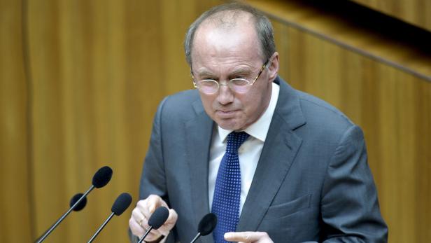Ein Mann mit Brille und Anzug spricht vor mehreren Mikrofonen.