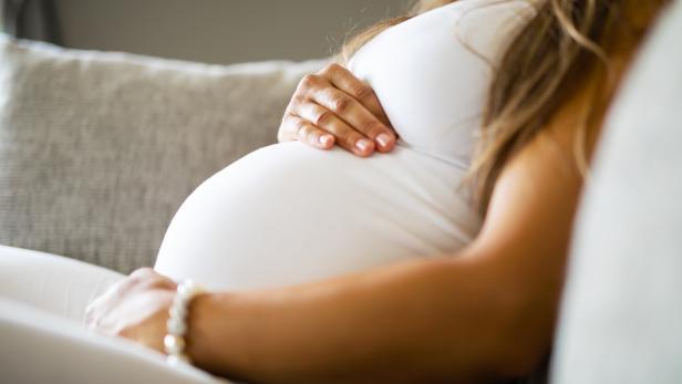 Close-up of pregnant woman sitting in sofa with her hands at belly