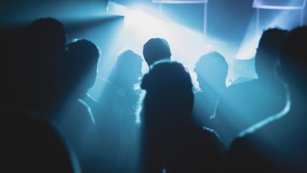 Silhouetten von Menschen stehen im blauen Licht einer Veranstaltung.