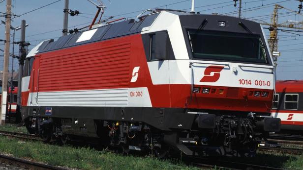 Eine rot-weiß lackierte Lokomotive der ÖBB steht auf einem Gleis.