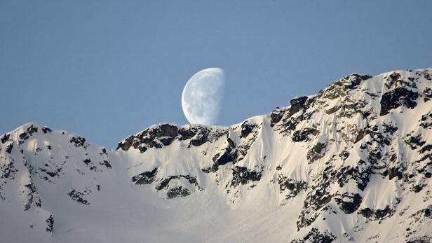 Ein schneebedeckter Berg unter einem hellen Halbmond.
