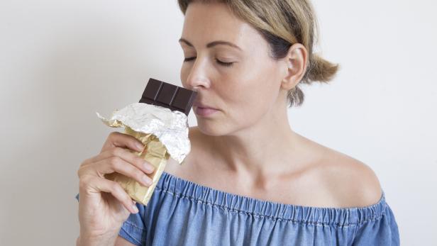 Portrait of a young beautiful girl with blond hair, bare shoulders and a neck, holding a chocolate bar to enjoy the taste. Sweet eating and organic products, a sense of temptation