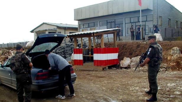 Ein Mann beugt sich über den Kofferraum eines Autos an einem bewachten Grenzübergang.