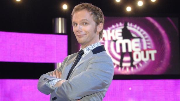 Ein Mann im Anzug steht vor dem „Take Me Out“-Logo.