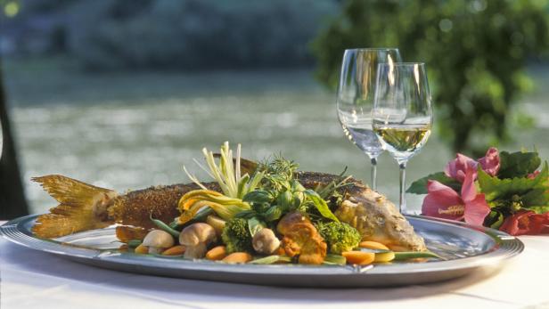 Ein zubereiteter Fisch mit Gemüse und zwei Gläsern Wein auf einem Tisch.