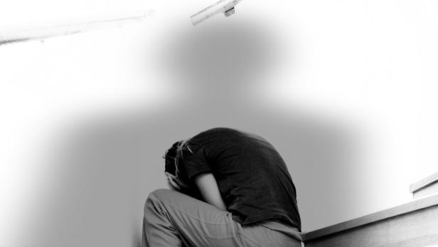 Eine Person sitzt mit gesenktem Kopf auf einer Treppe, die Hände vor dem Gesicht.
