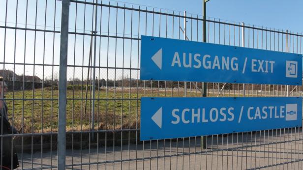 Schilder mit der Aufschrift „Ausgang“ und „Schloss“ an einem Zaun.