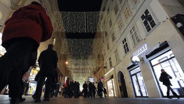 Eine abendliche Straße mit Menschen und Weihnachtsbeleuchtung in der Nähe eines „Breguet“-Geschäfts.