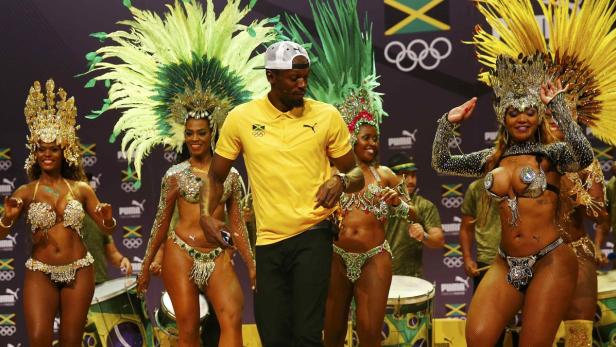 Usain Bolt umgeben von Tänzerinnen in Karnevalskostümen vor einem Hintergrund mit jamaikanischen und olympischen Symbolen.