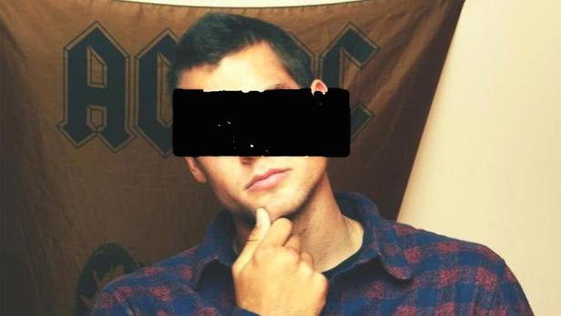 Ein Mann mit kariertem Hemd posiert vor einer AC/DC-Flagge.