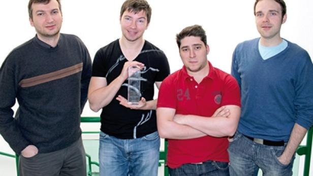 Vier Männer posieren für ein Foto, einer hält eine Trophäe.