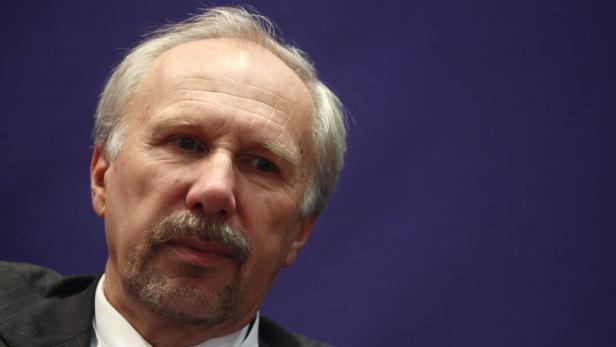 Porträt eines Mannes mit grauem Haar und Schnurrbart vor einem blauen Hintergrund.