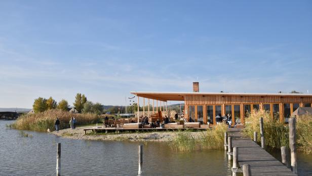 Ein Holzgebäude mit Terrasse steht am Ufer eines Sees, verbunden durch einen Steg.
