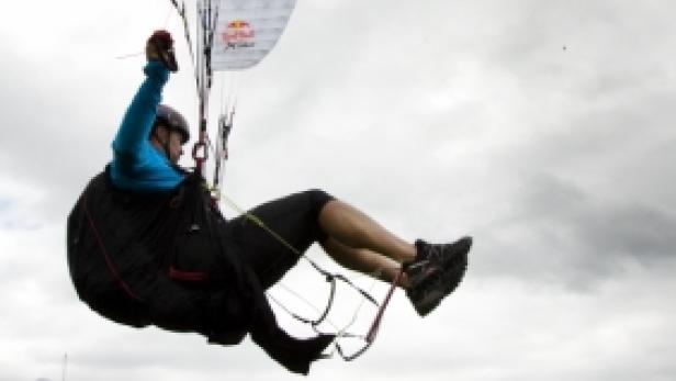 Ein Gleitschirmflieger führt einen Stunt vor einer Zuschauermenge auf einem Hügel aus.