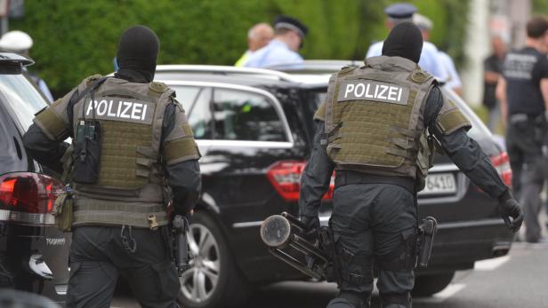 Zwei Polizisten in Kampfmontur stehen vor einem schwarzen Auto.