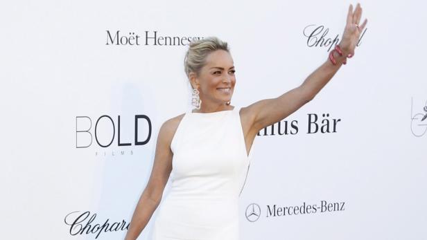 Sharon Stone in einem weißen Kleid winkt auf einer Veranstaltung.