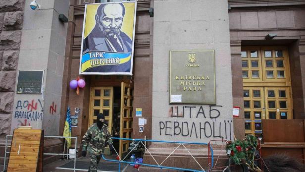 Ein Mann in Tarnkleidung betritt ein Gebäude mit einem Porträt von Taras Schewtschenko und Graffiti.