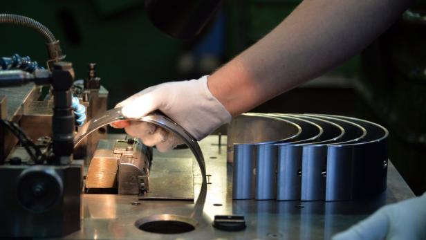 Eine Hand mit Handschuh bearbeitet ein Metallteil an einer Maschine.