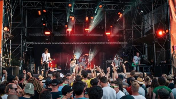 Rockband spielt vor großer jubelnder Menge auf einer Festivalbühne mit roten Lichtern.