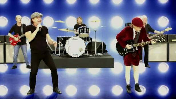 Die Rockband AC/DC tritt auf einer Bühne vor blauem Hintergrund auf.