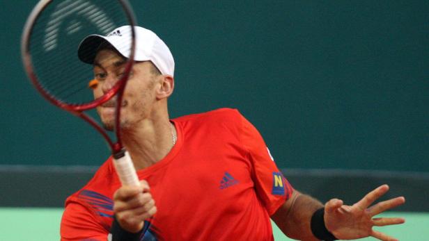 Ein Tennisspieler in rotem Hemd schlägt einen Ball mit seinem Schläger.