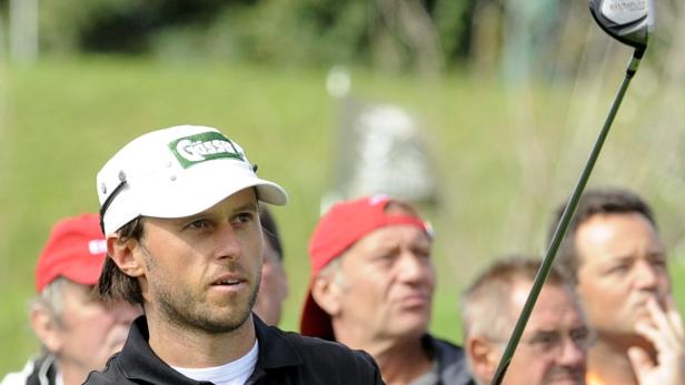 Ein Golfspieler mit weißer Kappe und Golfschläger im Anschlag, umgeben von Zuschauern.